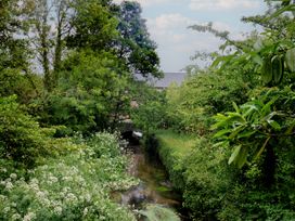 A view of a stream with trees and flowers near a bridge at 2 North Road, Maiden Newton, Dorset