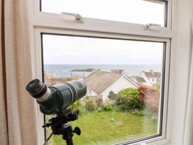 A telescope by a window with a view of the sea and houses at Wootton Gray in Penzance