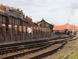 A train passing by houses and a speed limit sign near a railway station at Rails End 