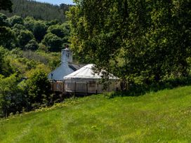 A yurt with a deck and chimney surrounded by trees at Hapus Yurt - Two Beautiful Yurts and Barn Cottage