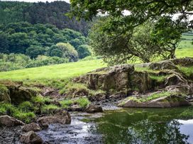 A nature scene with trees, grass, rocks, and a water pond at Hapus Yurt - Two Beautiful Yurts and Barn Cottage