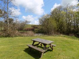 A picnic table in a grassy area with trees and a fence in the background at Riverside cottage with otters near Tintagel