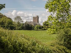 A church with a tower surrounded by trees and grass at Upper Frogpool Cottage in Crediton