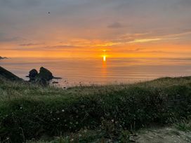 A sunset over the ocean with rocks in the foreground at Warleggan in Portreath