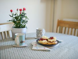 A kitchen table with scones, mugs, and a flower pot at Mead Cottage in Bridport