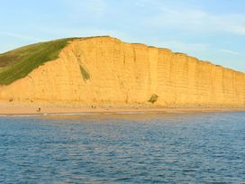 A beach with a cliff and people walking at Mead Cottage in Bridport