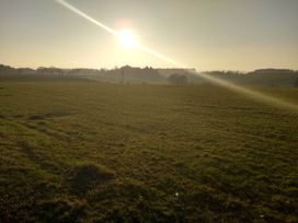 A field with sun setting behind trees and power lines at Cleeves Cabins 2, Arran Luxury Lodge with hot tub, St. John's Town Of Dalry