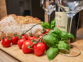 A kitchen scene with bread, tomatoes, basil, wine bottle, and glasses at Little Holm Garth 