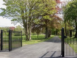 An open gate leading to a driveway lined with trees at Brettargh Holt Mansion near Levens