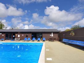 An outdoor pool area with deck chairs and a building at Hazelwood 3 Pinewood Retreat in Rousdon near Lyme Regis