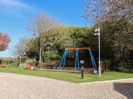 A swing set and benches in an outdoor area at Hazelwood 3 in Pinewood Retreat in Rousdon near Lyme Regis