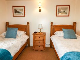 A bedroom with two beds and a nightstand with a lamp at Trelake Cottage in Tintagel