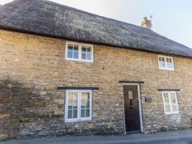A stone cottage with a thatched roof and windows at Honeypot Cottage in Weymouth