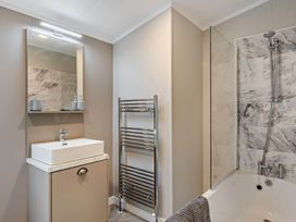 A bathroom with a wash basin, mirror, shower, and towel rail at Elwy 3.0 Pet, Llandyrnog