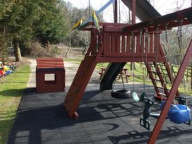 A play structure with slide, swings, and playhouse in an outdoor play area at Cider Cottage in Hawkchurch