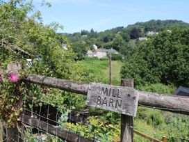 A sign on a fence indicating 'MILL BARN' with hills and trees in the background at The Mill Barn in Lustleigh