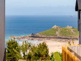 A beach view with a hill and lighthouse at Hidden 13- Skyline Terrace in St Ives
