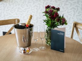 A dining table with a champagne bottle, glasses, flowers, chocolates, and a guest directory at Hidden 14- Garden Terrace, St Ives