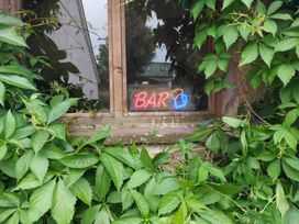 A window with a neon bar sign surrounded by green leaves at The Three Spaniels Shepherds Hut in Lampeter