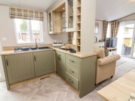 A kitchen with sink, stove, cabinets, and sofa at Hedgehog Lodge, Carnforth