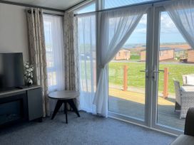 A living room with a TV and curtains at Stone Crab Lodge Hasguard Cross near Broad Haven