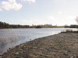 A view of a lake with a gravel shore and trees at Fanfare Superior at Three Lochs Holiday Park Newton Stewart