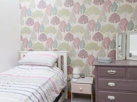 A bedroom with a bed, bedside table, lamp and drawer chest at 2 Bryn Eglwys in Prenteg