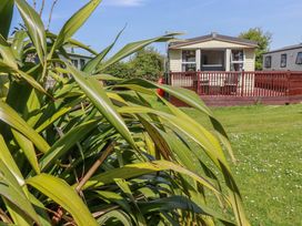 A mobile home with a wooden deck surrounded by grass at Beech Lodge in Wadebridge
