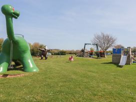 A playground with a dinosaur structure, monkey structure, swing set, slide, and playhouse at Beech Lodge in Wadebridge