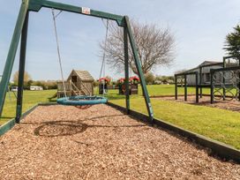 A playground with a swing and playhouse at Beech Lodge in Wadebridge