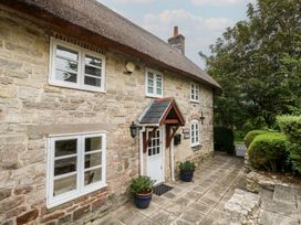 A stone cottage with a thatched roof and pathway at Woodbine Cottage in Weymouth