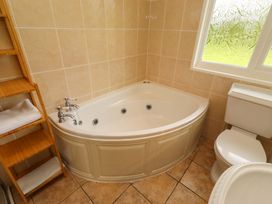 A bathroom with a bathtub, toilet and shelves at Campden in Rennington near Embleton