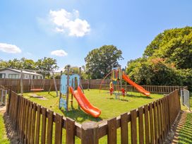 A playground with slides swings and grass at Forest Retreat - FO26 Saxmundham
