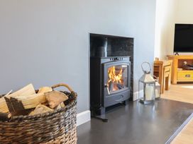 A wood stove with a fire and a wood basket at Tyn Y Weirglodd in Deiniolen