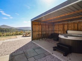 An outdoor patio with a hot tub and wooden furniture at Tyn Y Weirglodd in Deiniolen