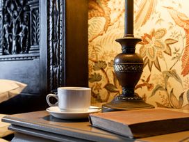 A bedside table with a coffee cup, lamp, and book at Lonsdale House Bowness-On-Windermere