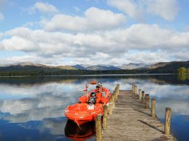 A boat docked on a wooden pier with mountains and water in the background at Lonsdale House Bowness-On-Windermere