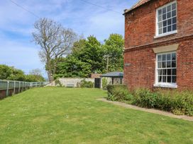 A garden with grass, trees, and a bench at Reighton House in Filey