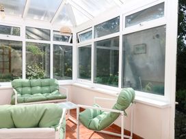 A conservatory with green sofas and glass windows at Gorway Cottage in Teignmouth