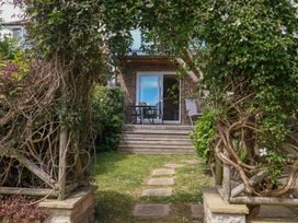 A garden with a pathway leading to a patio area at Little Gem in Weymouth
