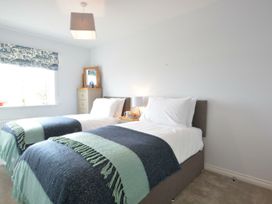 A bedroom with two beds, a nightstand, and a window at Lapwings, Aldeburgh