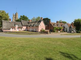 A row of thatched and pink houses with a church tower at The Annex in Cavendish Near Sudbury