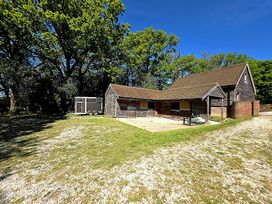 A barn and stables with trees in the background at Charming Barn Annex with Stables New Forest Escape