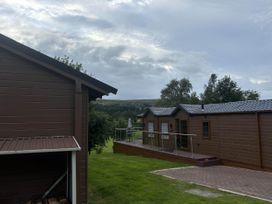 An outdoor view of a wooden cabin and deck at Pet Friendly - Lodge at Riverview Holiday Park Mangerton near Newcastleton
