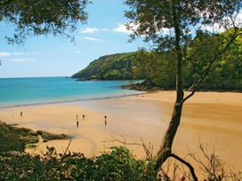 A beach scene with people walking on sand and water at 6 Knowle Court in Salcombe
