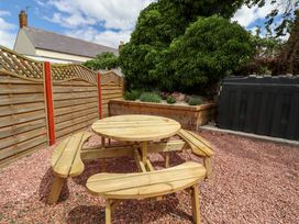 A garden with a wooden table and benches surrounded by gravel and a planter at Sarah's Cottage
