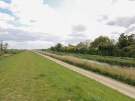 A grassy path along a waterway with trees at Laurel in Littleport