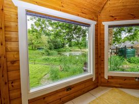 A sunroom with large windows showcasing views of a pond and greenery at Bull Rush Cabin Carwinley near Longtown
