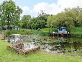 A pond with a dock and small cabin at Bull Rush Cabin Carwinley near Longtown