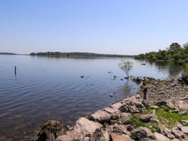 A lakeside view with rocks and trees at Mayfly Cottage 